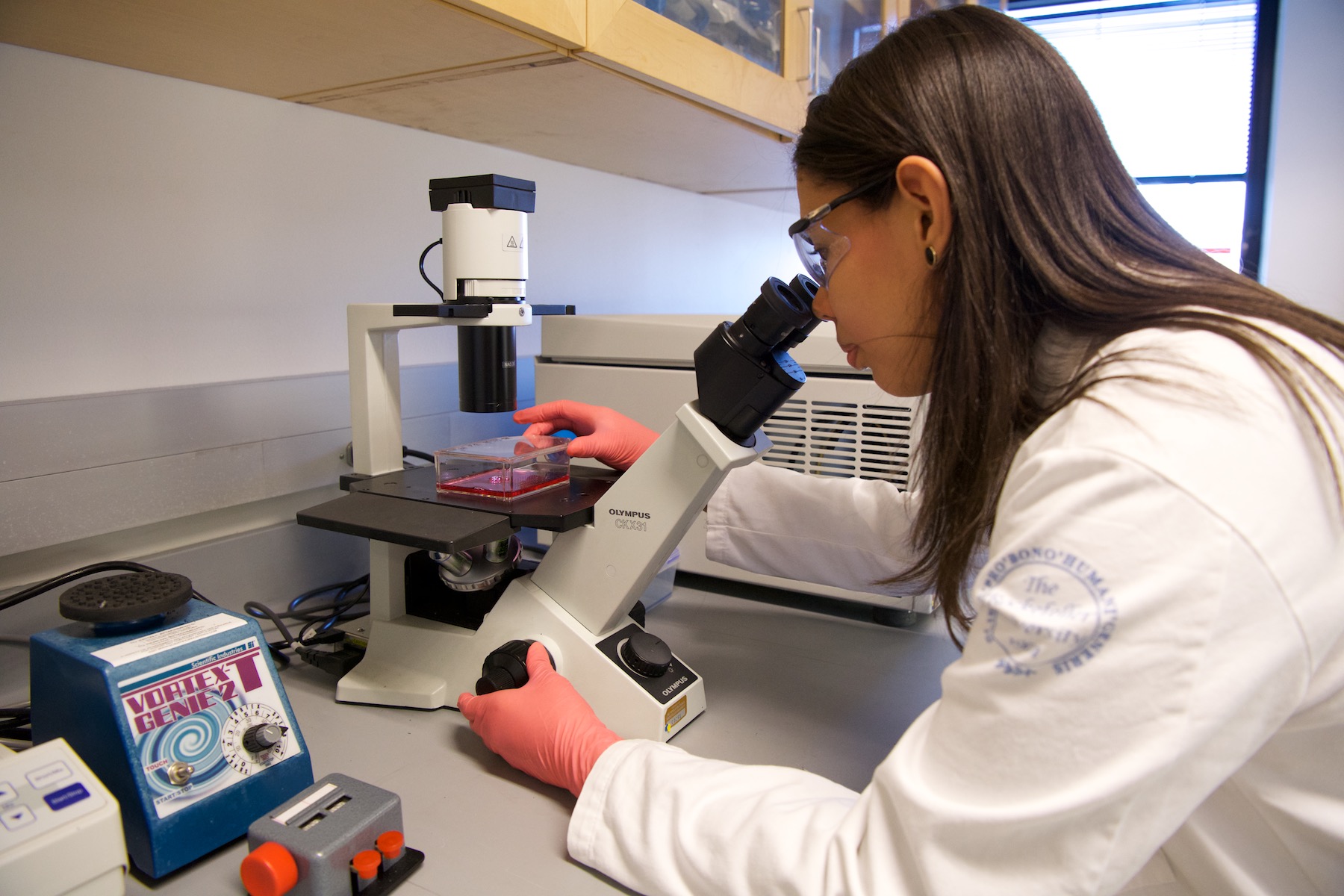 Claudia Melo, BMCC alumna, sitting at a microscope in a lab.