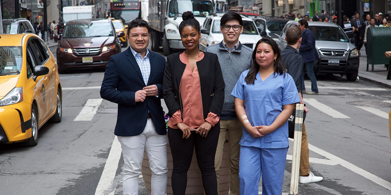 four students, one in scrubs, standing in street
