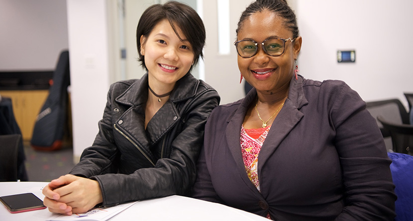 two women students sitting at a table smiling