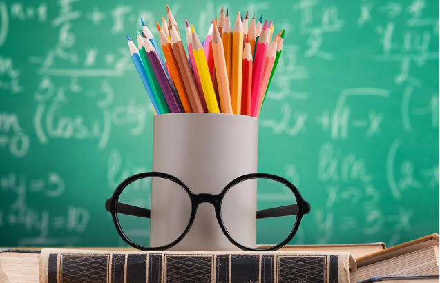 pencils in a cup on some books with a blackboard in the background, covered with formulas