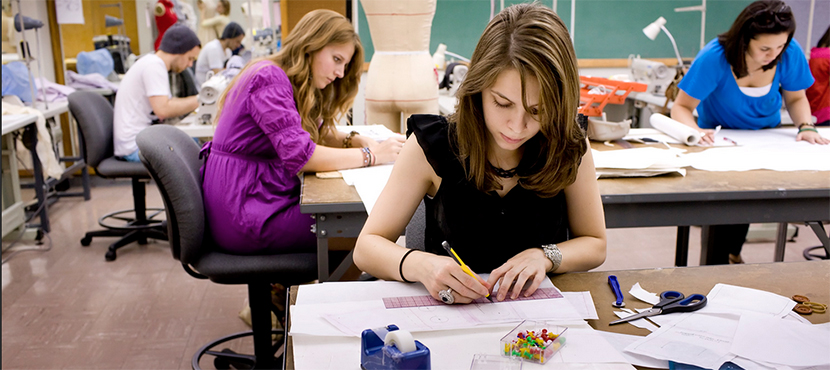 students working on fashion design projects at tables in a classroom