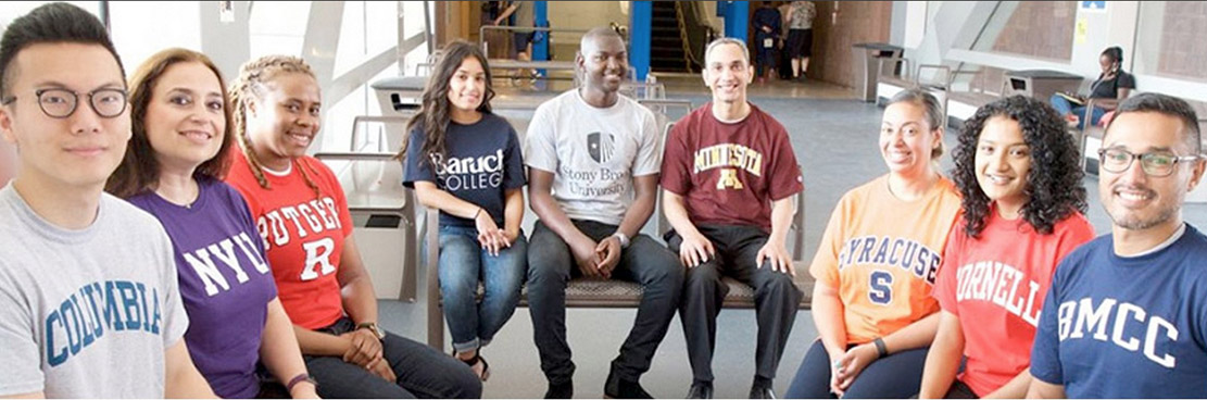 Students wearing the tee shirts of different colleges, sitting on chairs in a semi-circle