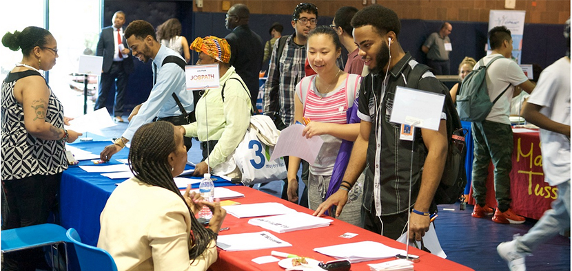 Career Fair in the BMCC gym -- students gathered at a table with flyers, speaking to representatives from different companies
